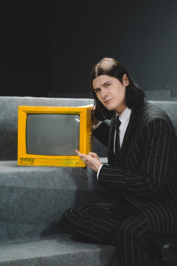A young man in a retro suit pointing at a vintage yellow TV, studio setting.