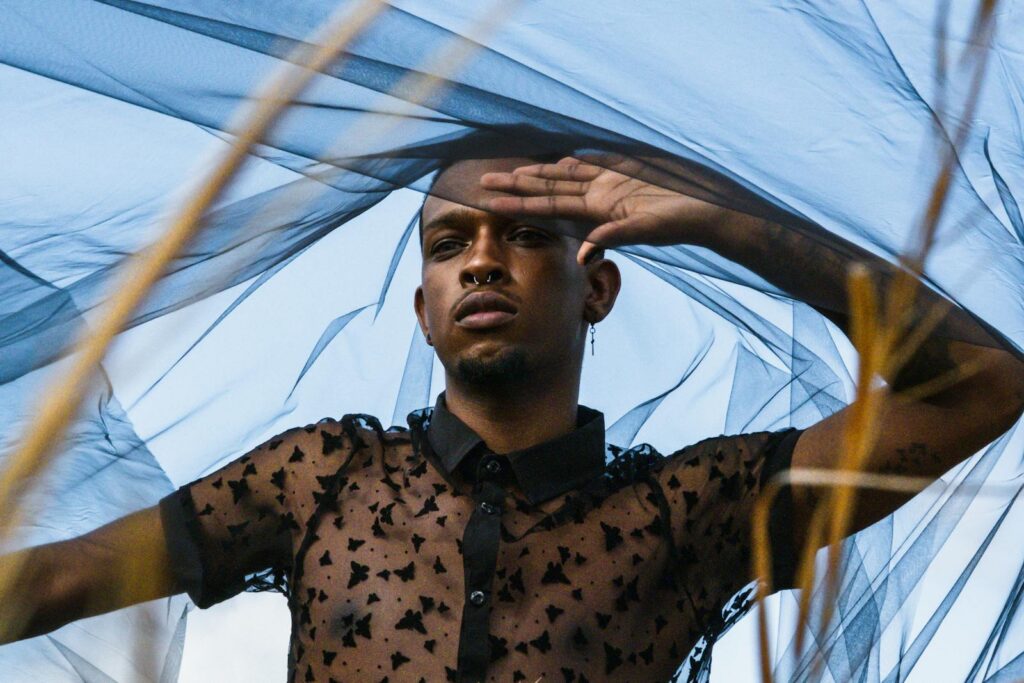 Man posing with sheer veil and modern fashion in outdoor setting.