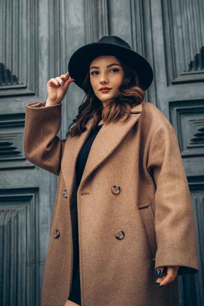 Stylish woman posing in a cashmere coat and wide-brimmed hat against a textured background in Türkiye.