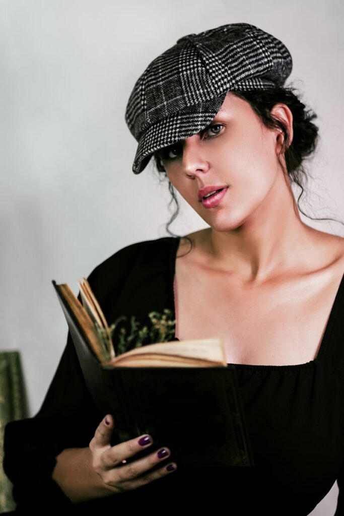 A young woman wearing a newsboy cap reads a book in an artistic vintage setting.