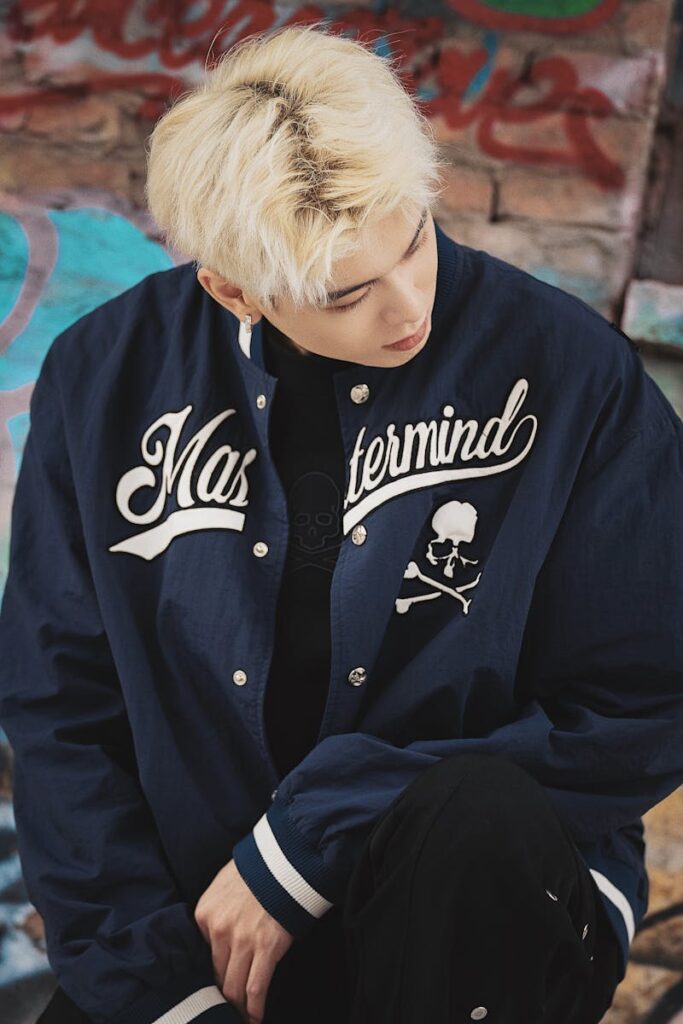 Stylish portrait of a blonde man in a blue jacket against graffiti background.