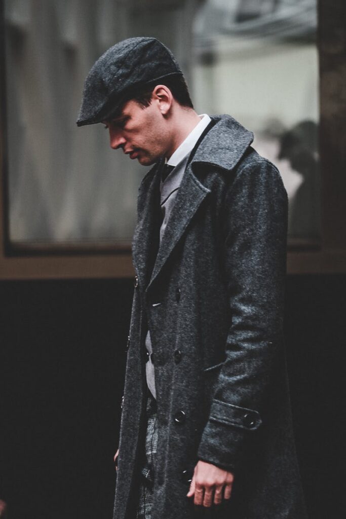 Stylish man in grey coat and cap walking along a city street, embodying classic fashion.