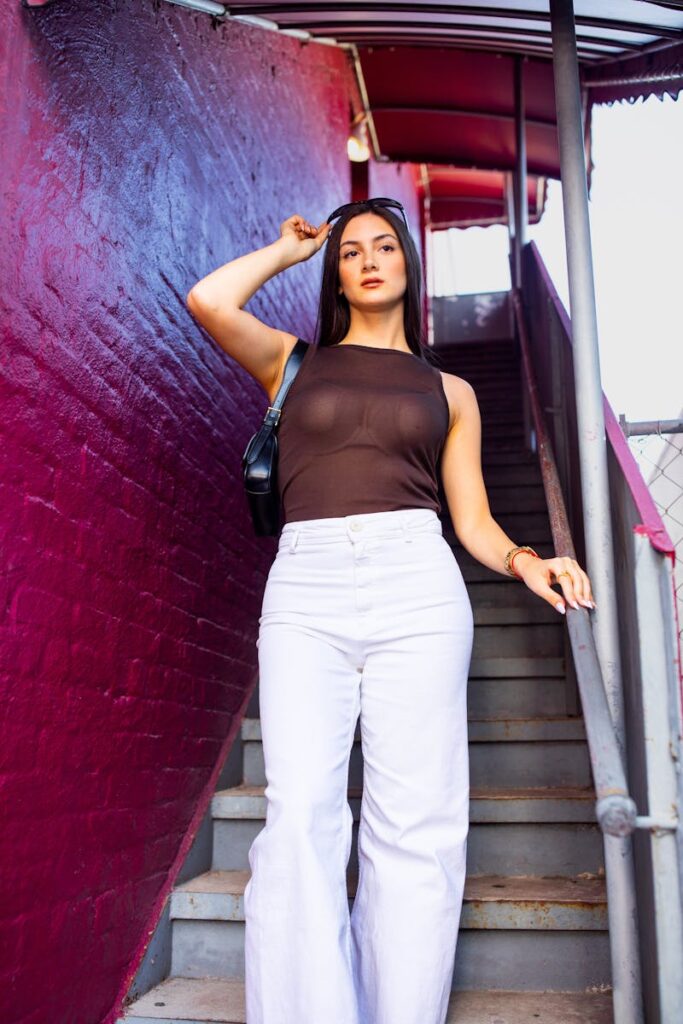 A fashionable woman poses confidently in white jeans on a vibrant urban staircase.