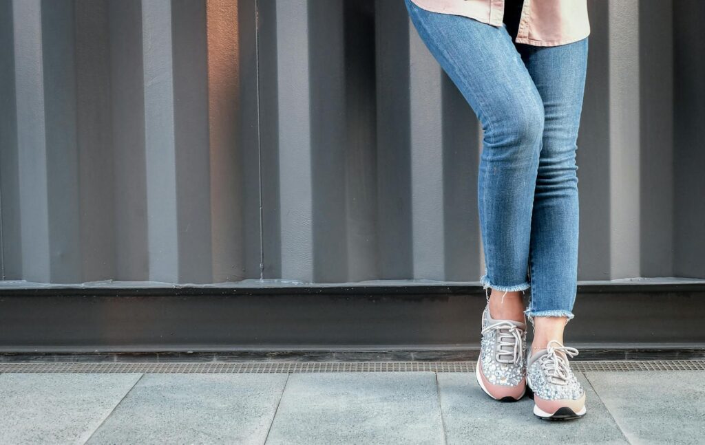 Stylish woman in jeans and glitter sneakers leans casually outdoors.