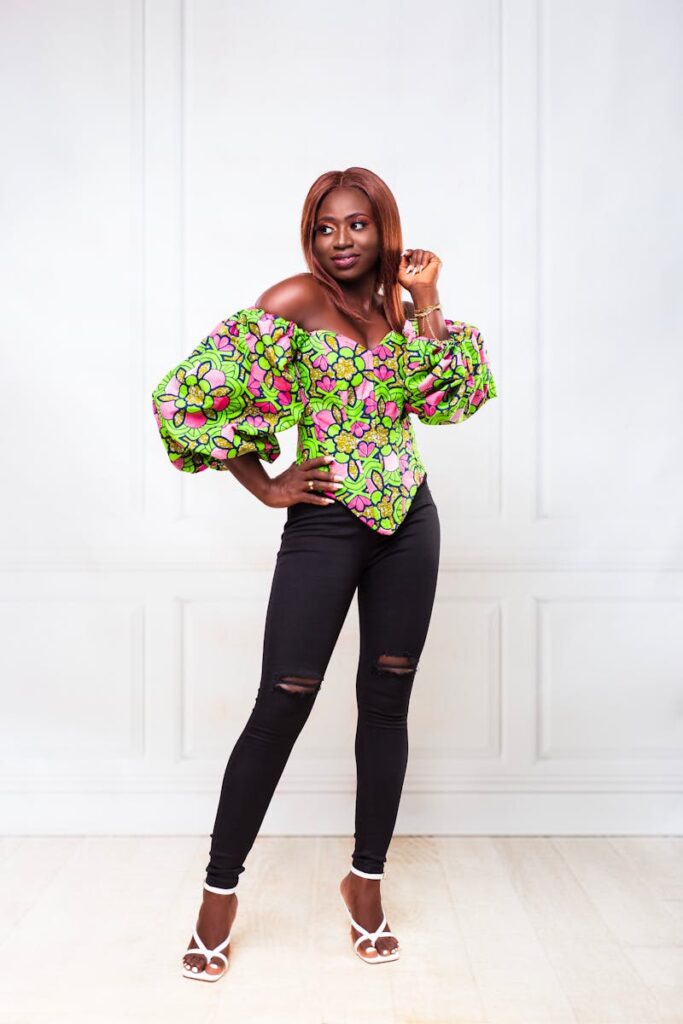Stylish woman wearing a vibrant floral blouse and black pants posing gracefully indoors.