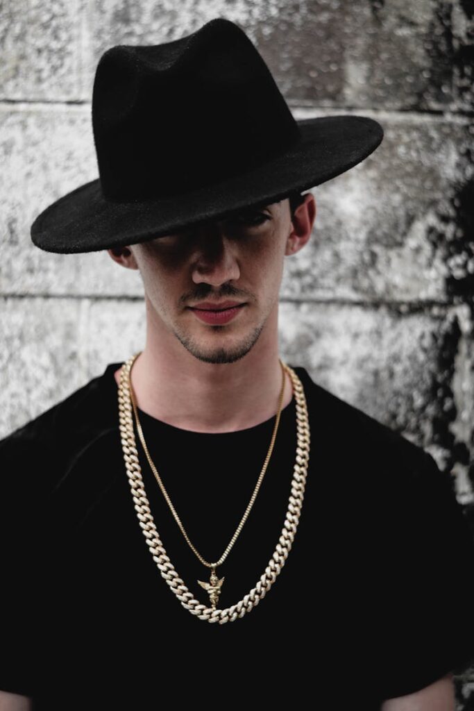 Portrait of a fashionable man wearing a black hat and gold chains against a textured background.