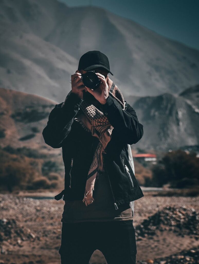 A photographer in dark attire taking pictures in a mountainous terrain during the day.