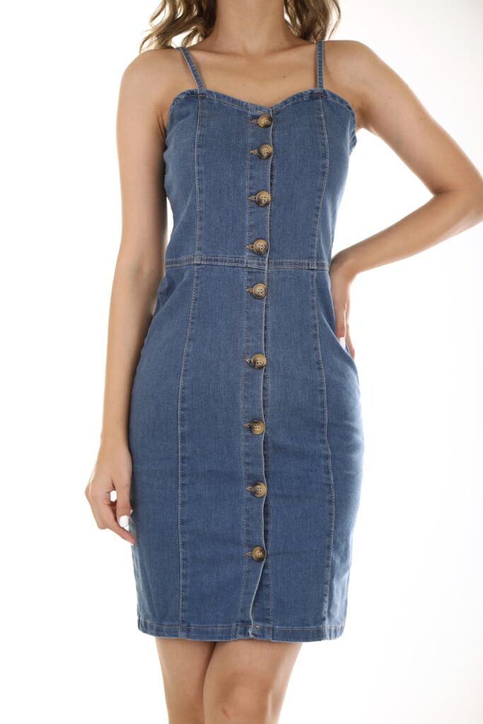 Stylish sleeveless denim dress with button-front detail against a white background.