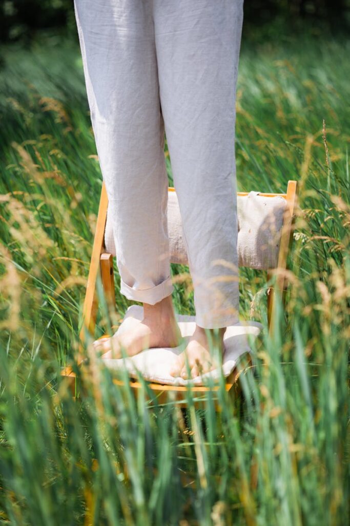 Barefoot person standing on a chair in a sunny summer field, embodying relaxation and leisure.