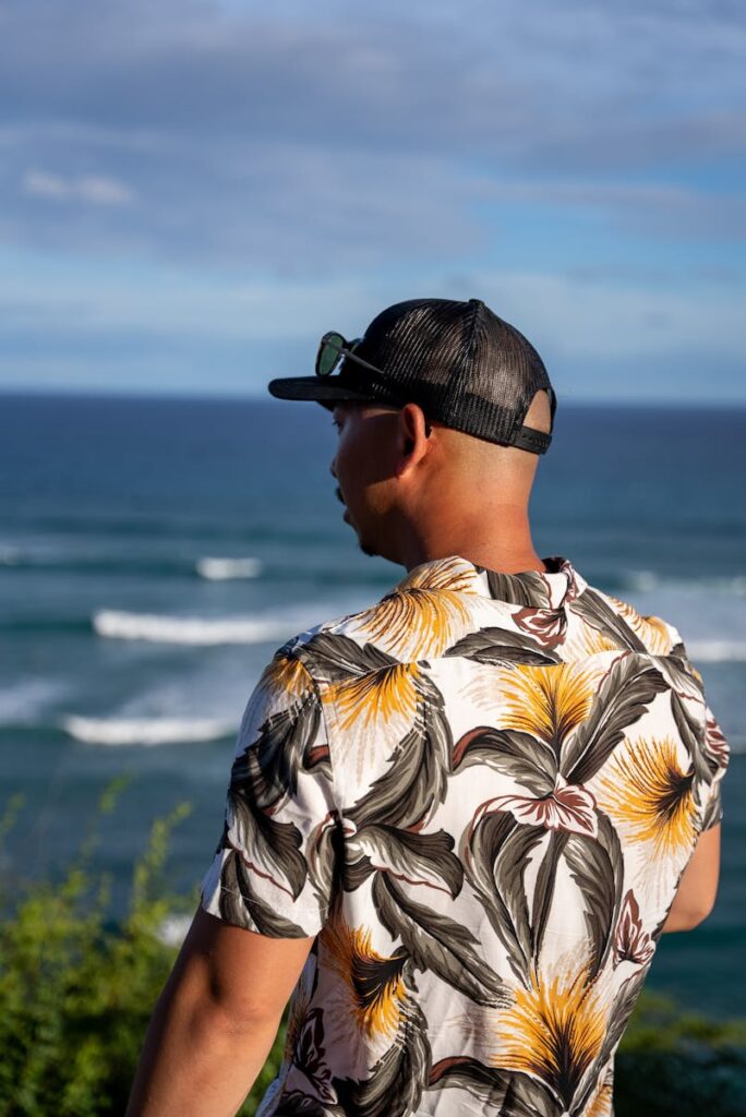 Man wearing a floral shirt and cap overlooking the ocean in Honolulu, Hawaii.