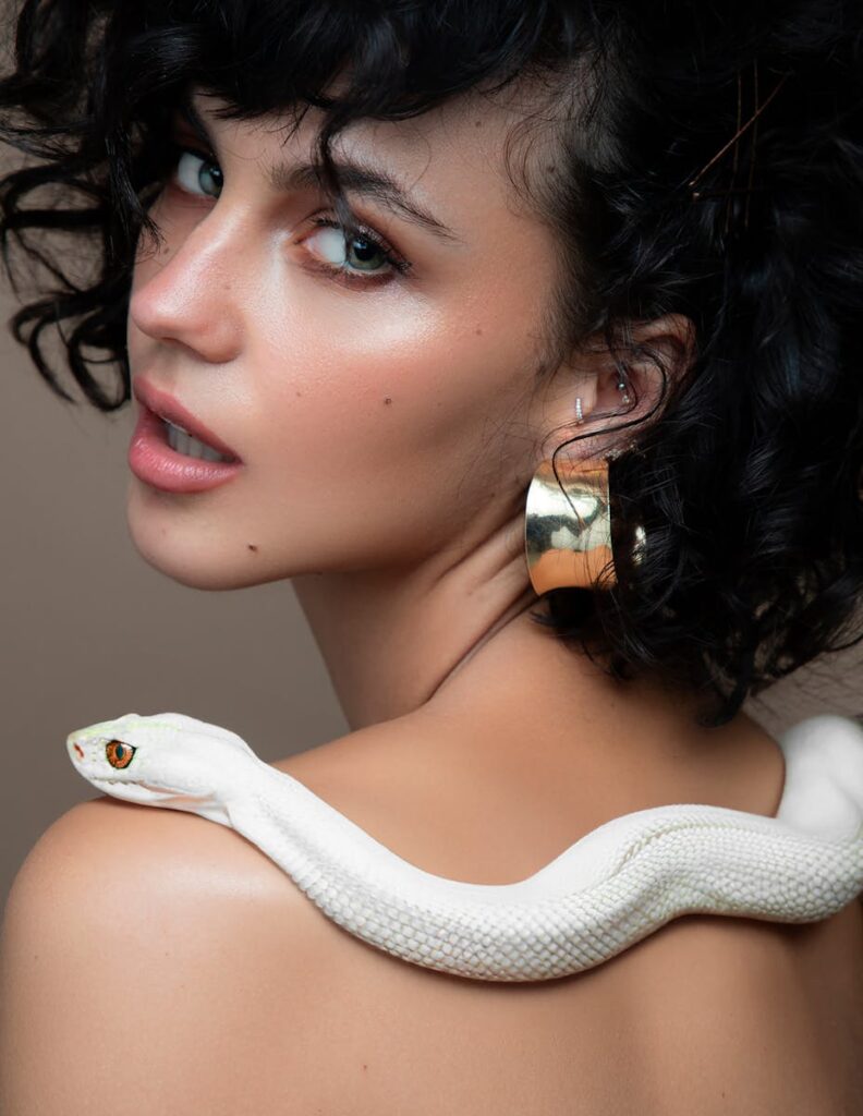 A woman posing elegantly with a white snake on her shoulder, showcasing grace and allure.