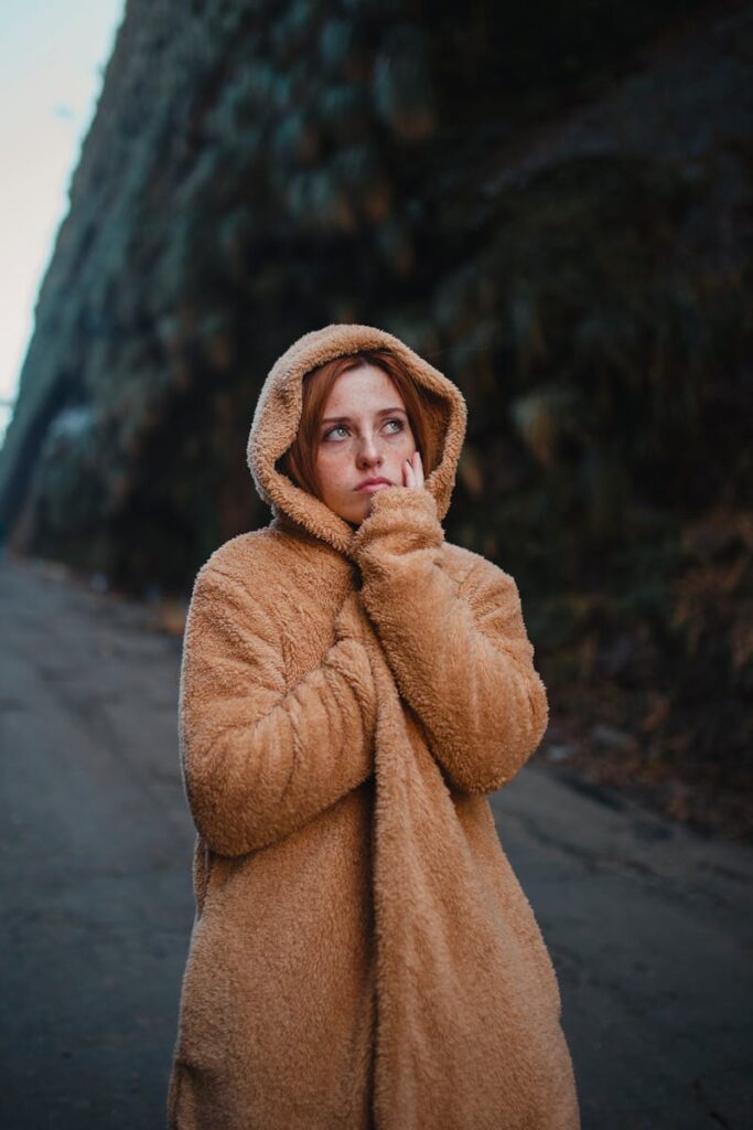 A thoughtful woman in a warm hooded coat stands outdoors, exuding coziness and style.