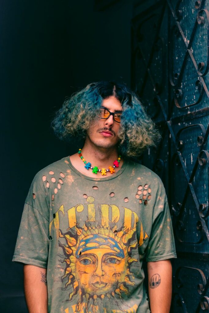 Stylish portrait of a man wearing a distressed tee with colorful hair and a vibrant necklace.
