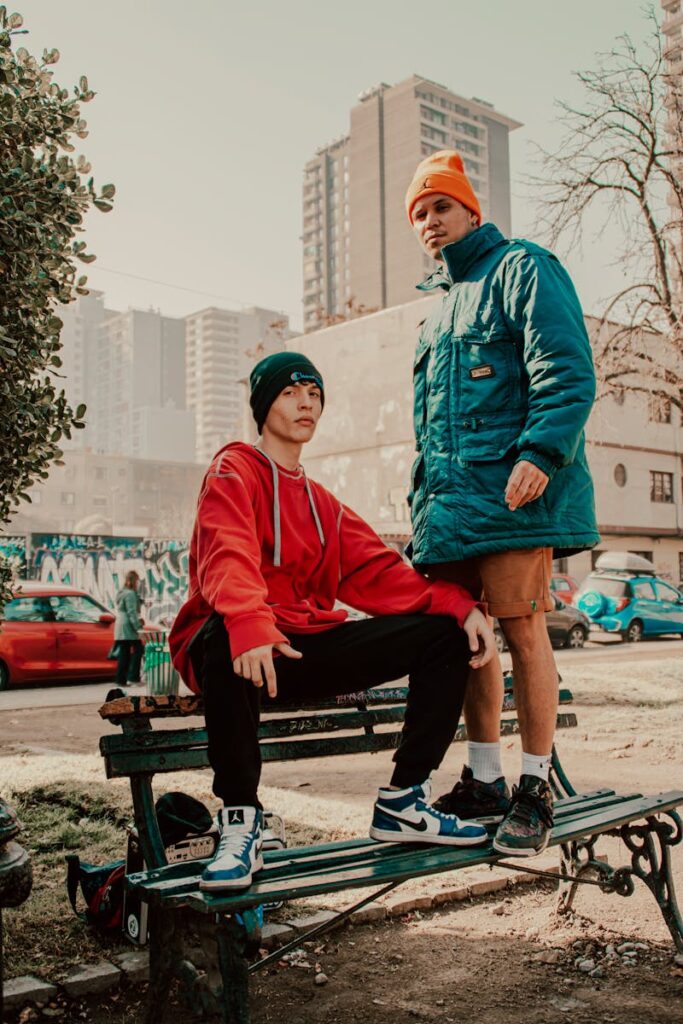Two young men flaunt urban fashion on a city street bench, showcasing modern streetwear.