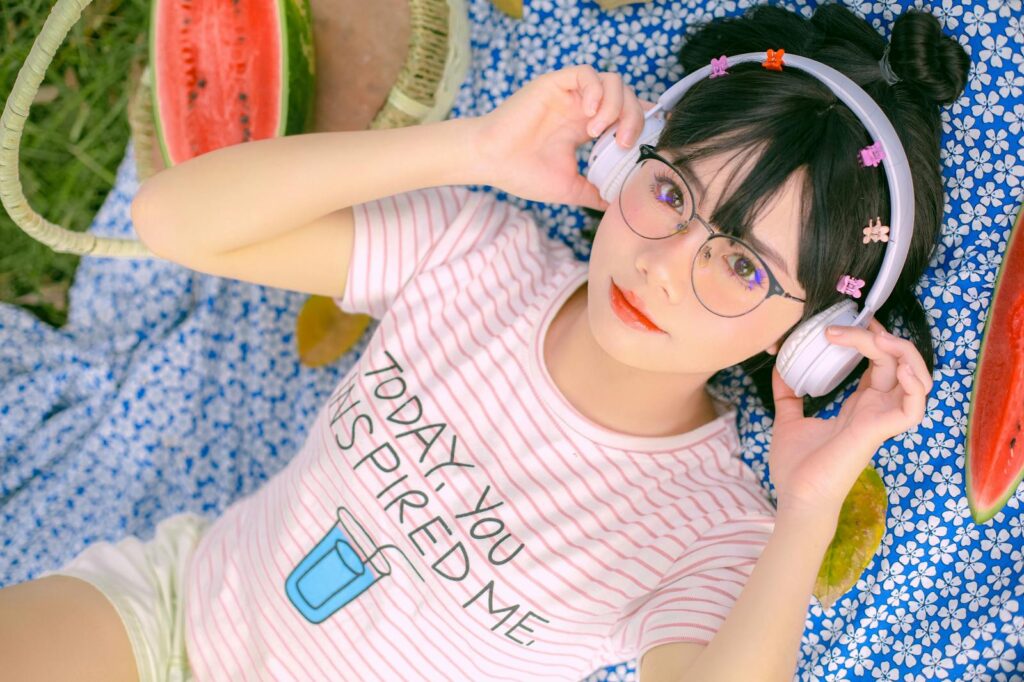 Teenage girl relaxing on a picnic blanket, listening to music with headphones, enjoying summer vibes.