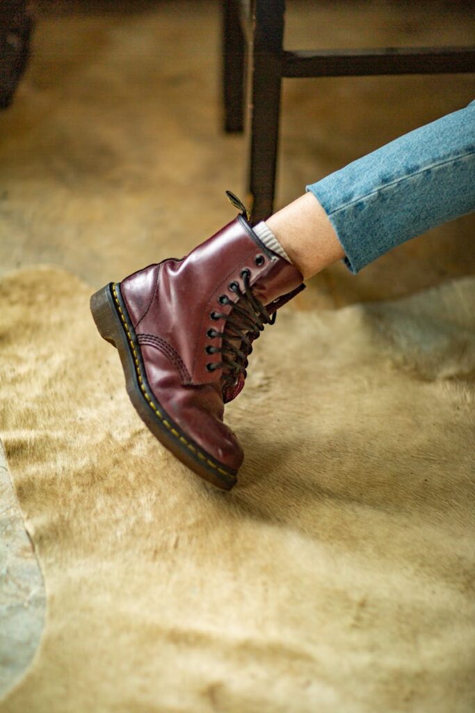 Close-up of a stylish burgundy leather boot with laces on an indoor beige rug.