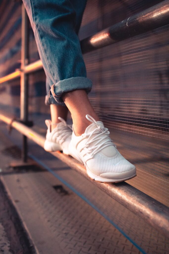 Close-up of white sneakers over a metal railing, showcasing casual style and urban fashion.