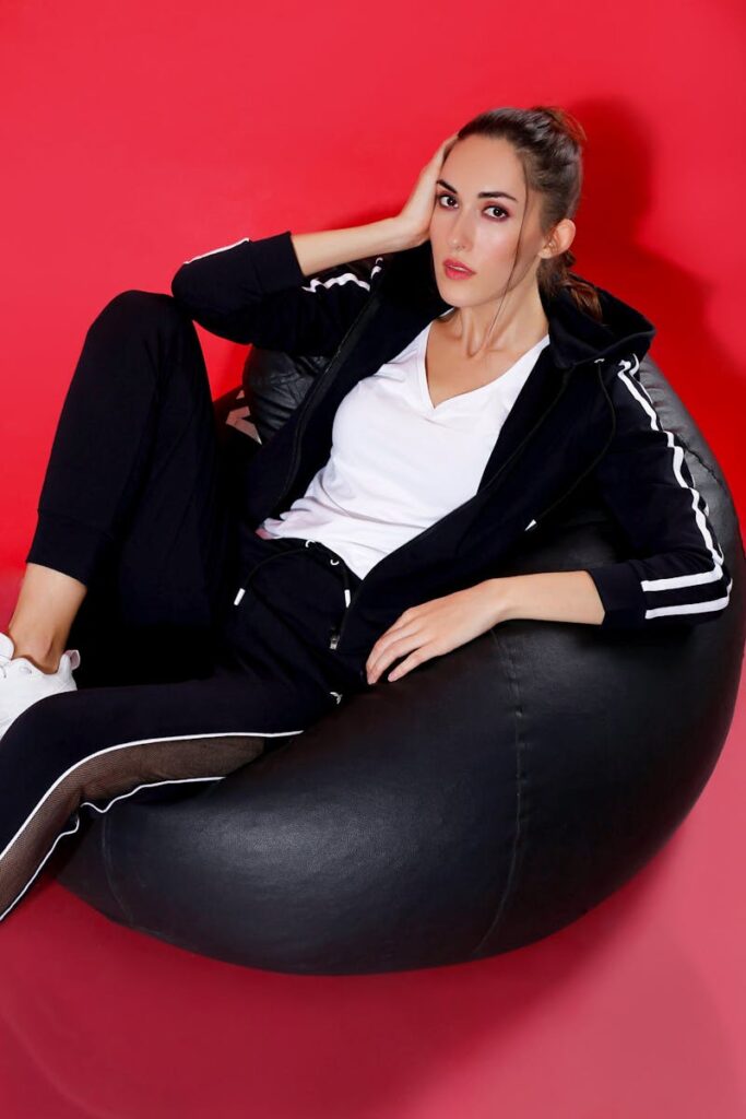 Young woman in sporty outfit lounging on a black bean bag against a vibrant red backdrop