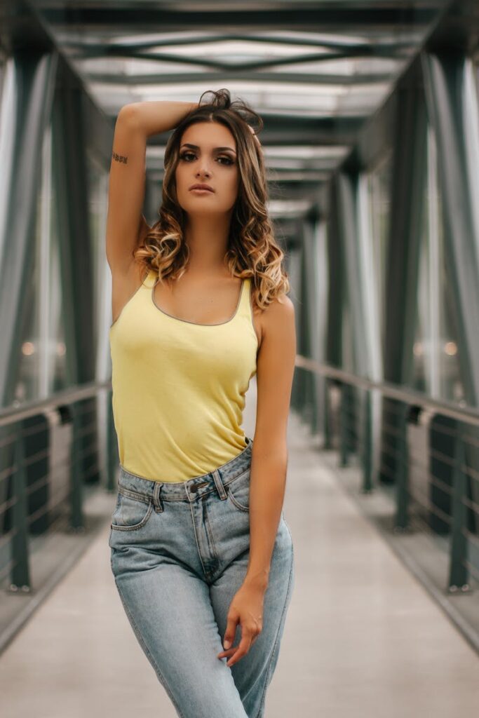 Portrait of a stylish woman in a yellow tank top posing confidently in a modern urban environment.