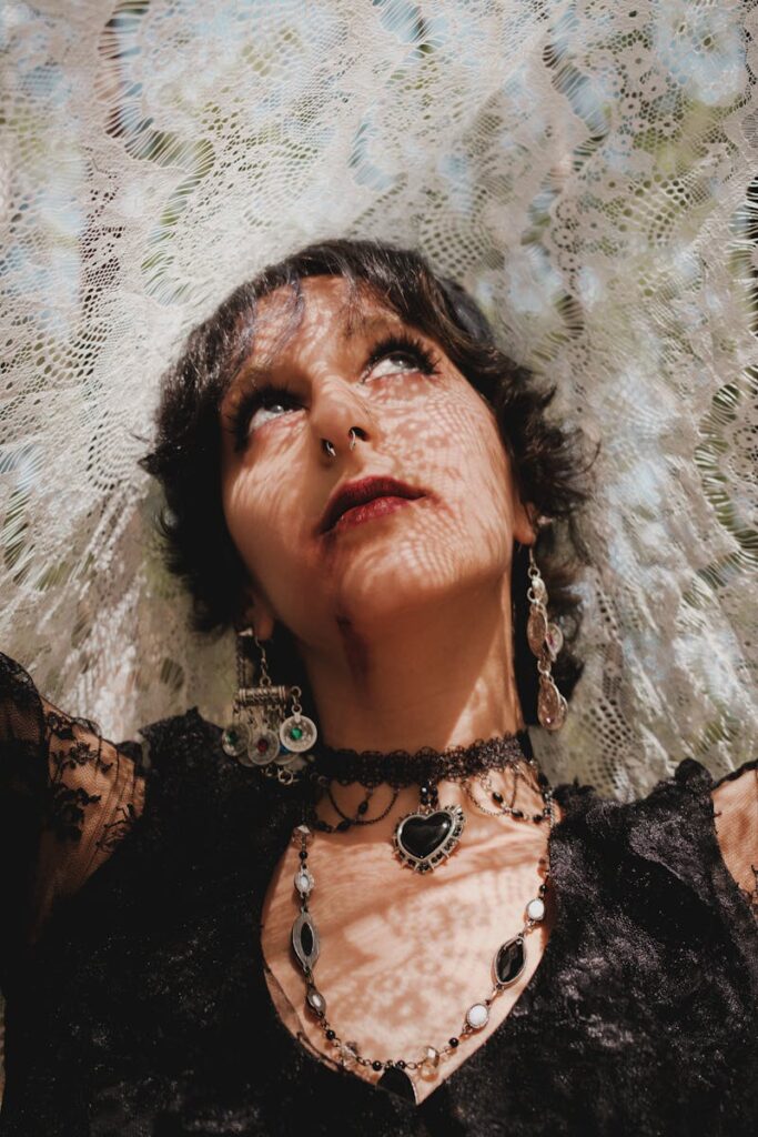 Artistic portrait of a woman wearing intricate jewelry under a lace veil, casting delicate shadows.