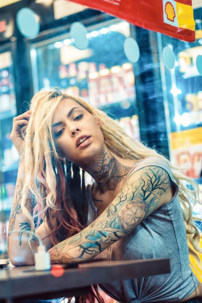 Edgy tattooed woman with blonde dreads posing in a modern cafe atmosphere.