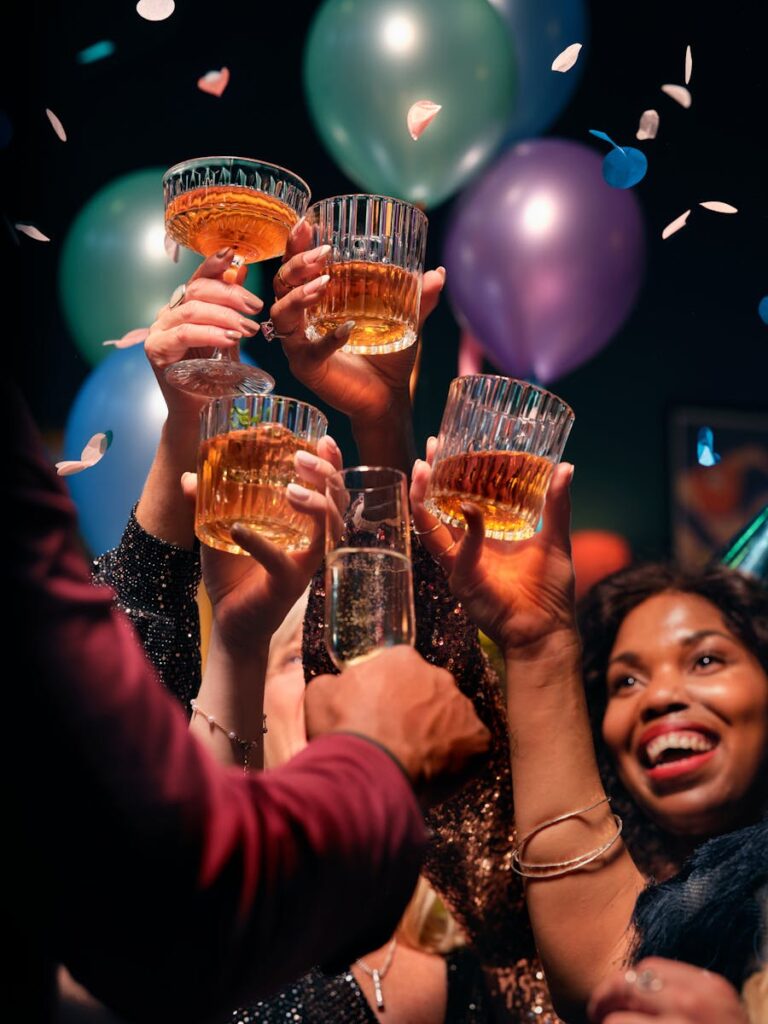 Group of friends raising glasses in a joyful toast, celebrating with balloons and confetti.