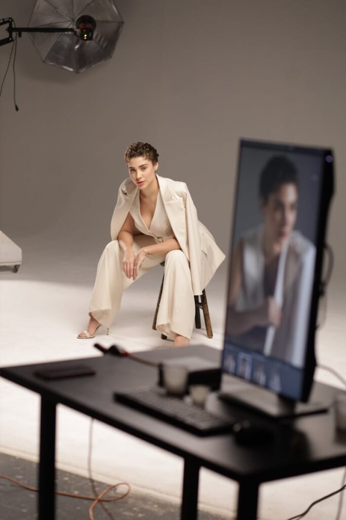 Elegant studio photoshoot featuring a fashionable model sitting on a stool in a minimalist setting.