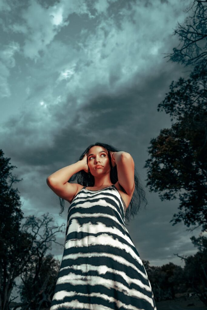 A stylish woman poses confidently outdoors against dramatic storm clouds.