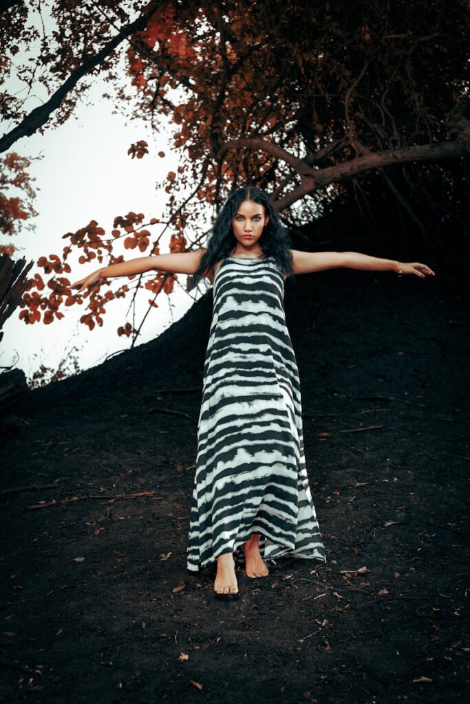 A young woman in a striped dress poses outdoors, embracing fall's natural beauty.