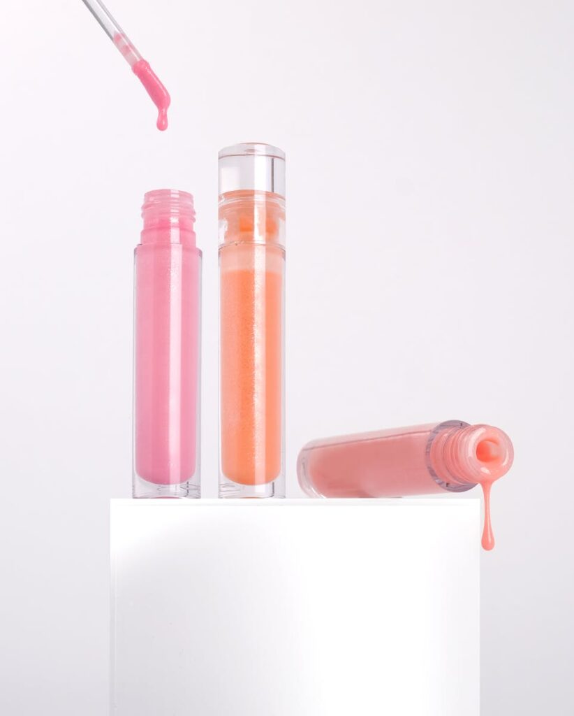 Colorful lip gloss tubes with dripping liquid on a white background for cosmetic products.
