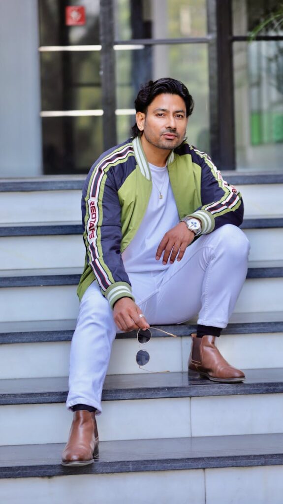 Man wearing green bomber jacket and chelsea boots sitting on steps, showing urban casual style.