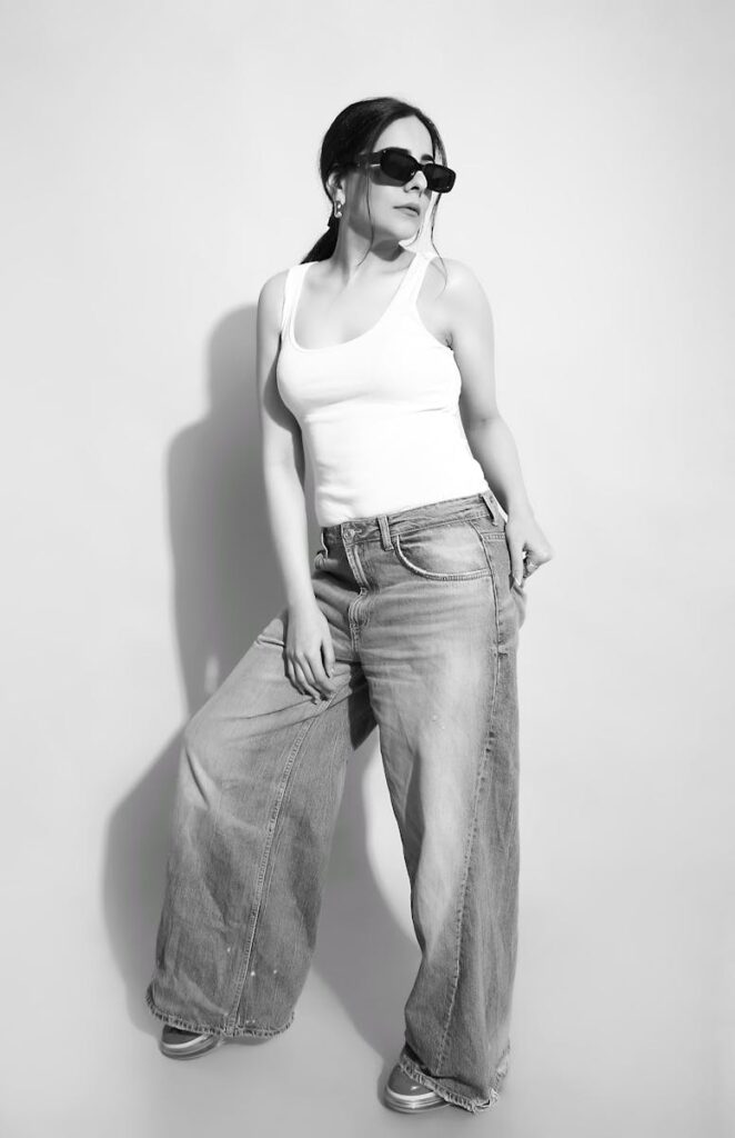 Chic woman in wide-leg jeans and sunglasses posed confidently against a white background.
