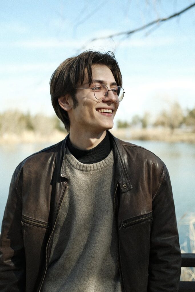 Smiling young man wearing a leather jacket near a river in fall.