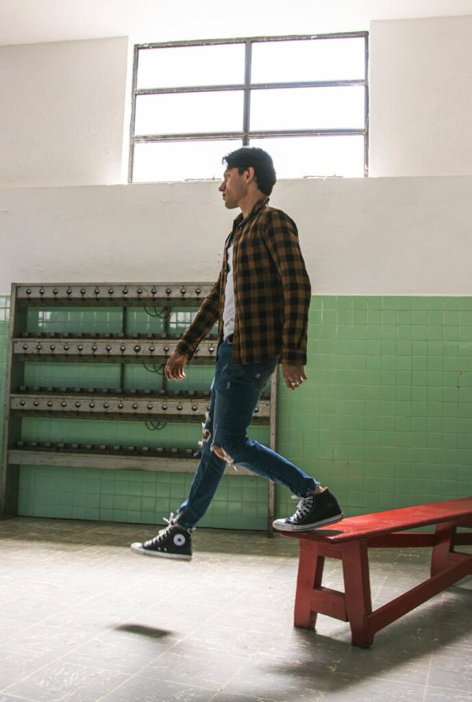 Stylish young man in midair over a red bench, wearing checkered shirt and distressed jeans.