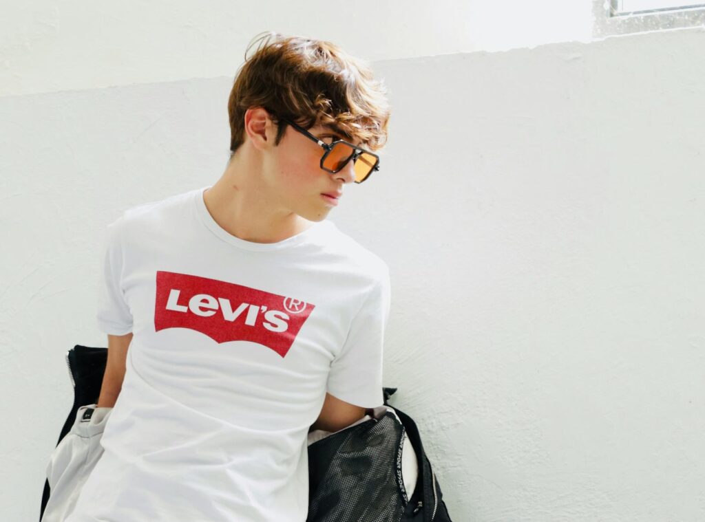 Stylish young man wearing Levi's t-shirt with sunglasses against a white background.