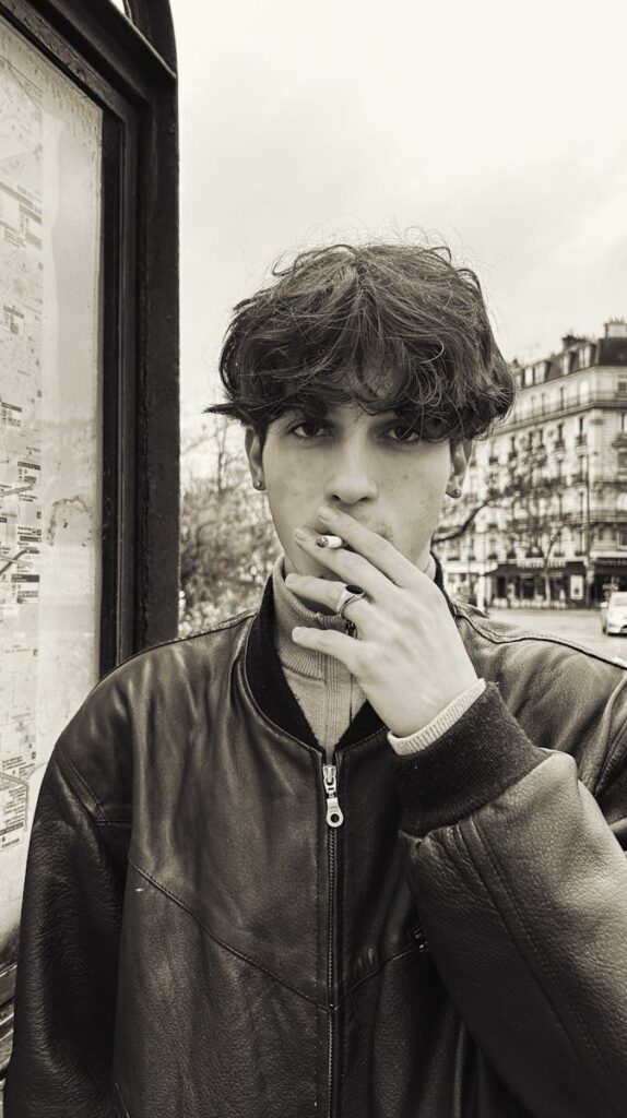 Young man with a leather jacket smoking in the streets of Paris. Urban fashion vibe.