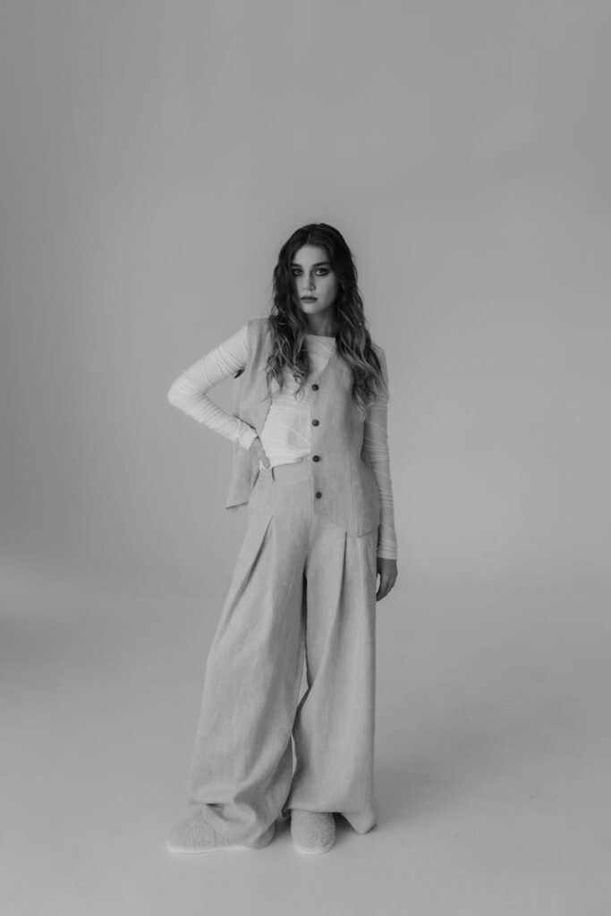 Black and white portrait of a woman wearing bell bottoms posing in a studio.