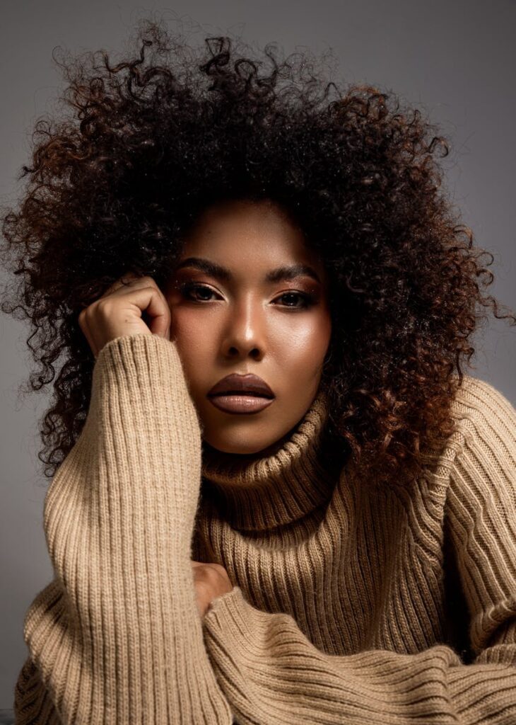 Close-up portrait of a woman in a beige knit sweater, showcasing elegant makeup and natural curls.