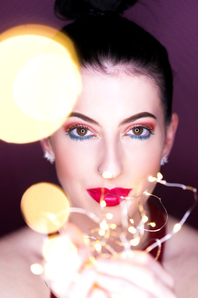 Captivating close-up of a woman with vibrant makeup and fairy lights, creating a glamorous effect.