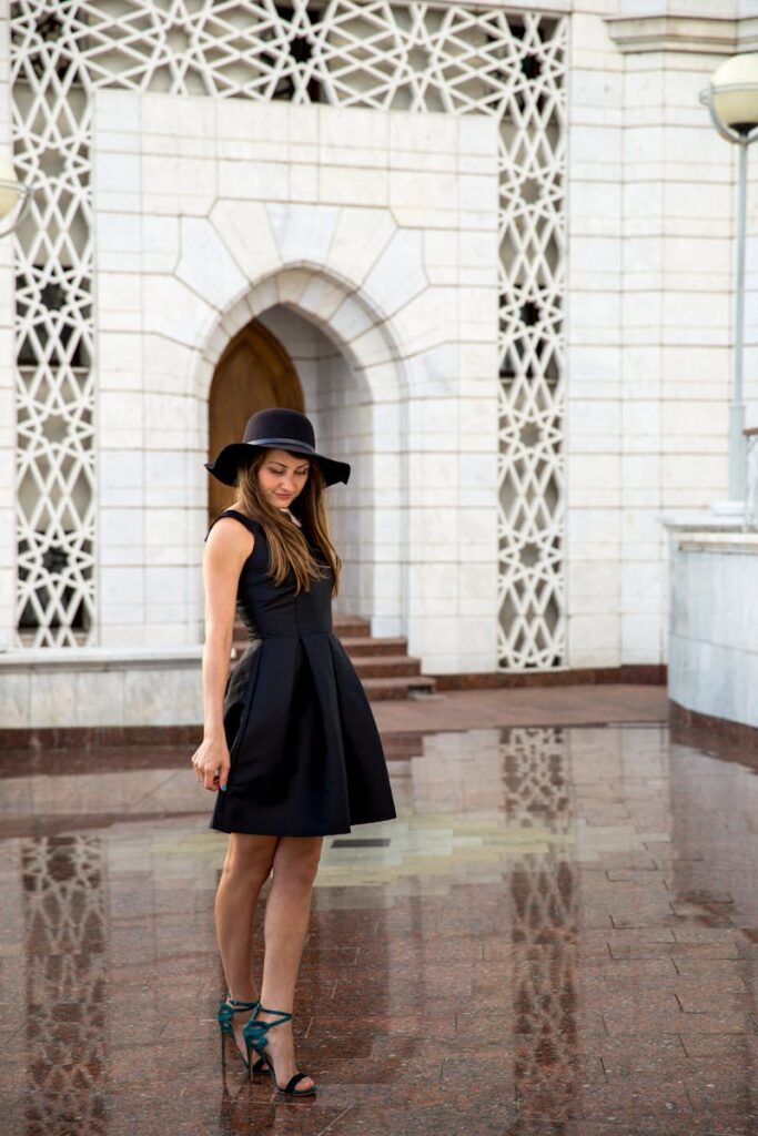 Elegant woman in a black dress posing outdoors by a decorative building.