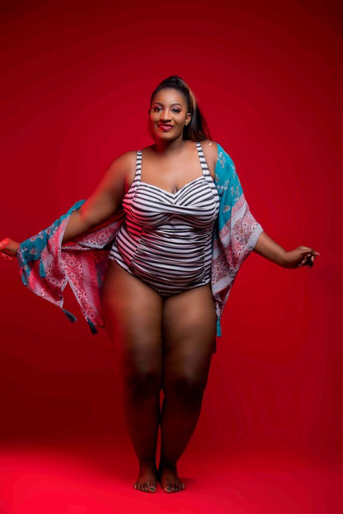 Stylish woman in a striped swimsuit with a kimono posing confidently against a red background.