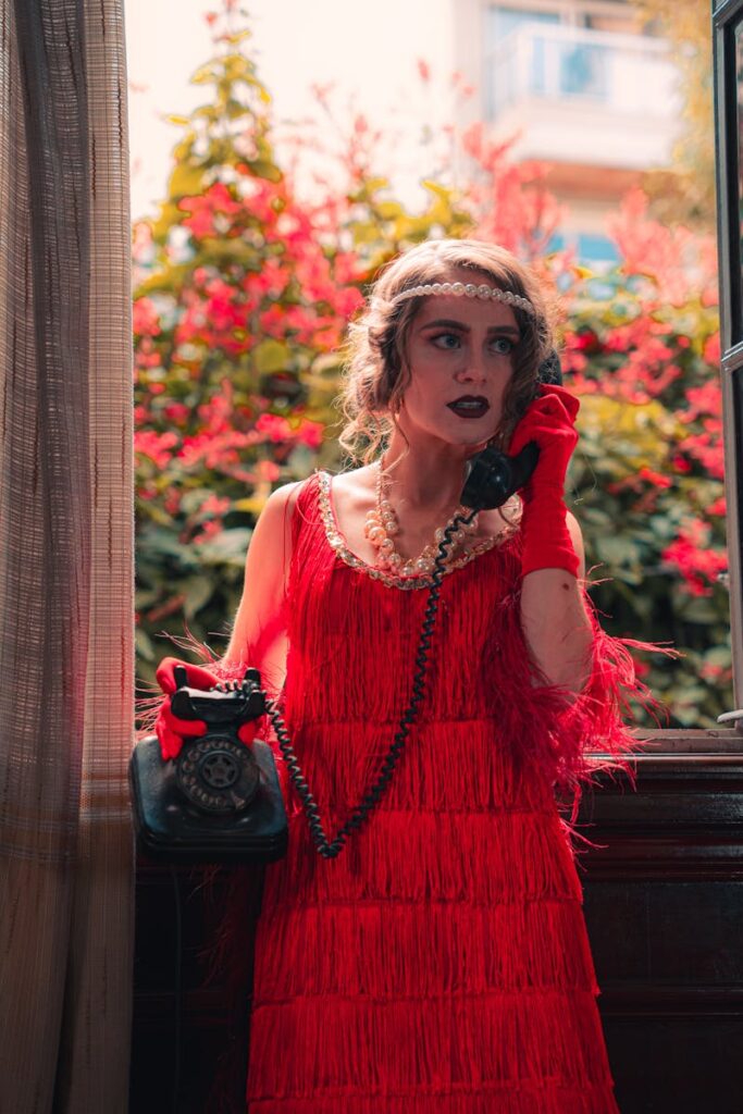 Stylish woman in a 1920s flapper dress using a vintage telephone indoors.