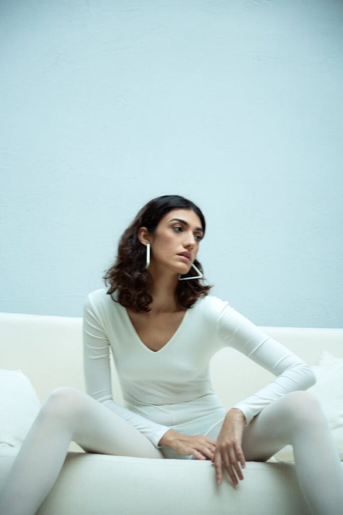 Stylish portrait of a woman in white attire seated on a sofa, exuding elegance.