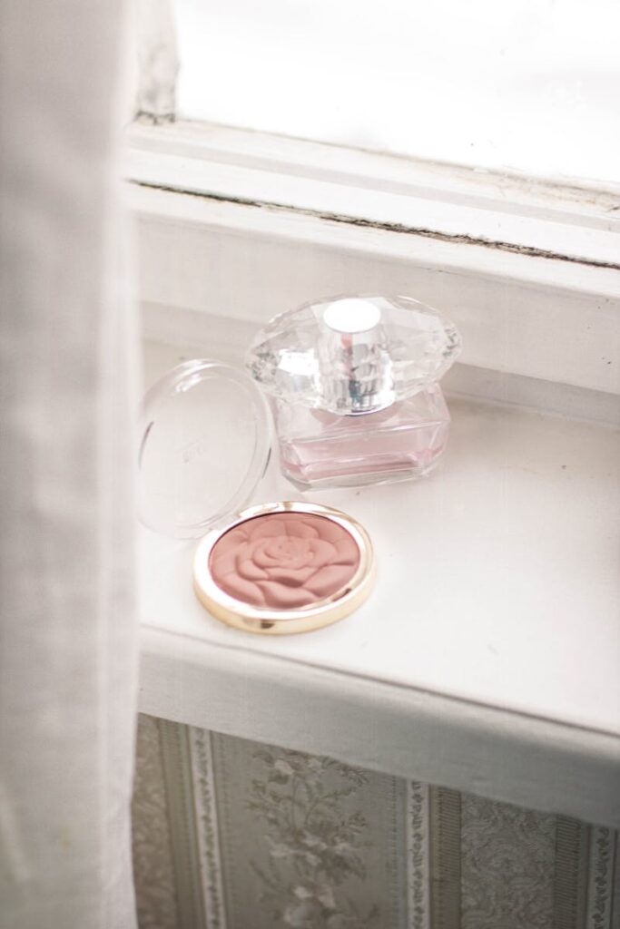A delicate perfume bottle and blush in a rose pattern on an elegant windowsill create a vintage and chic atmosphere.