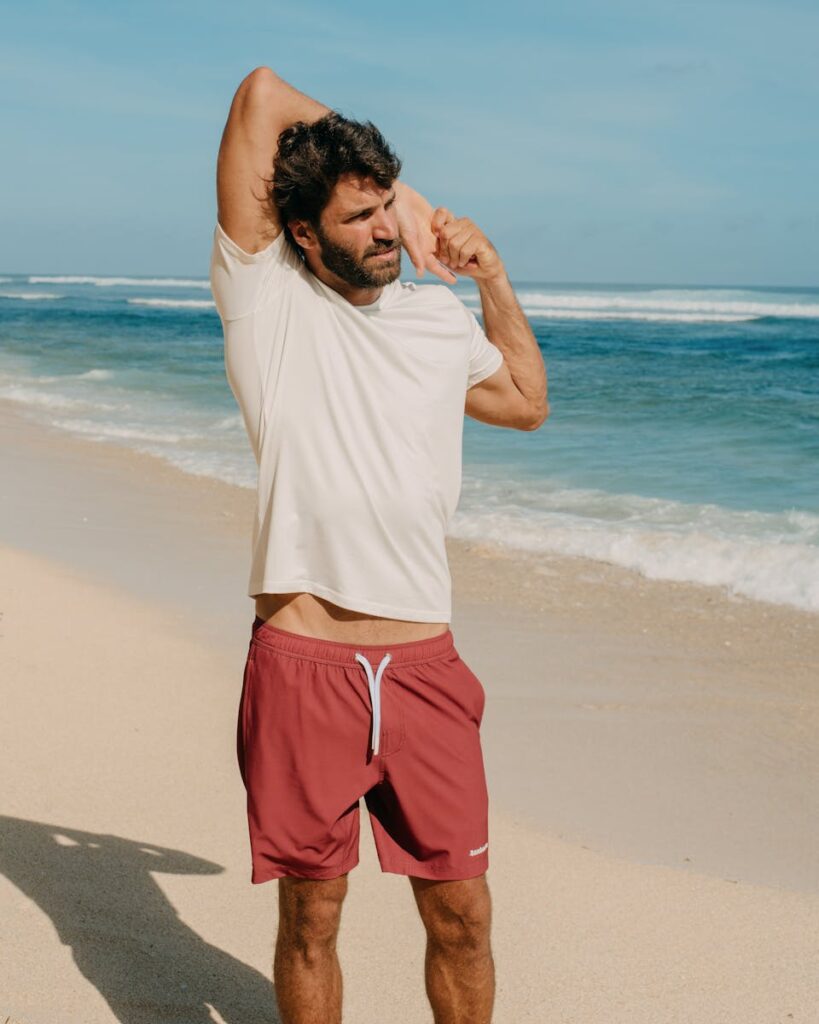 Athletic man stretching on a sandy beach wearing casual sportswear under the clear sky.