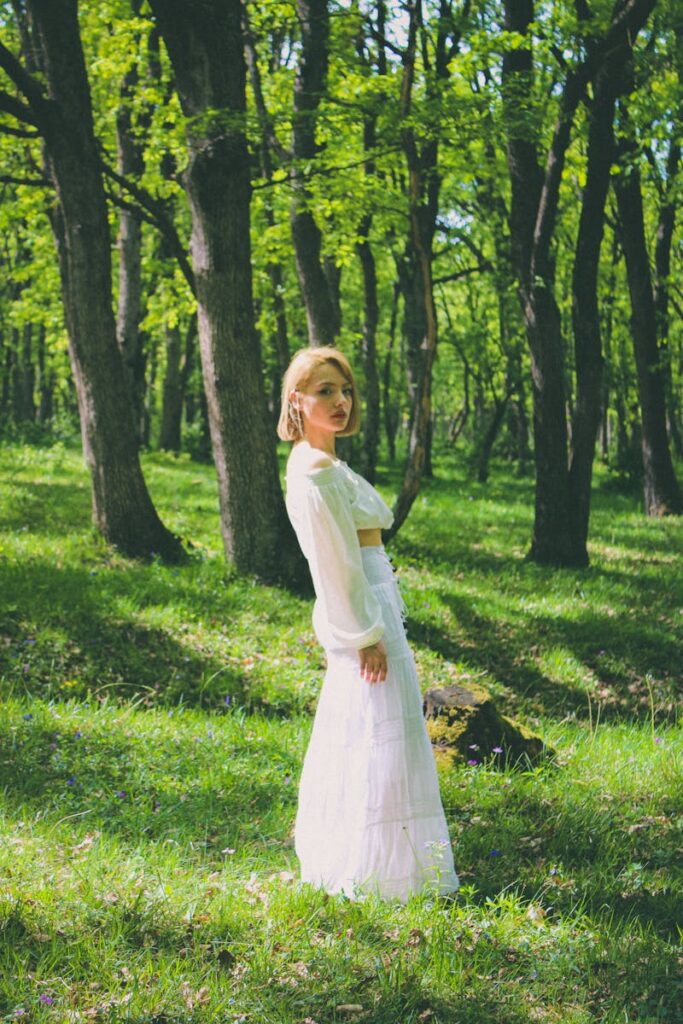 A woman in a white outfit stands gracefully in a sunlit forest clearing, exuding tranquility.