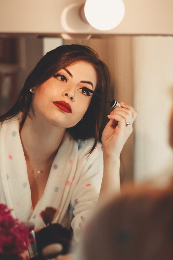 Glamorous woman applying mascara in front of a vanity mirror, enhancing her beauty.