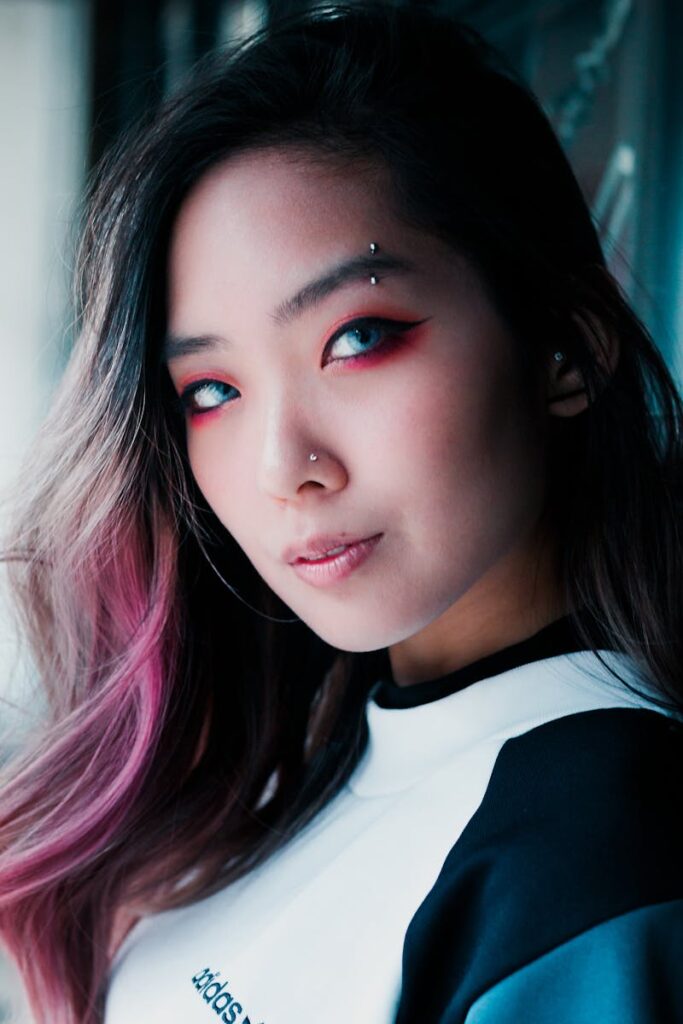 Stylish portrait of an Asian woman with vibrant eye makeup and pink hair highlights, showcasing modern fashion.