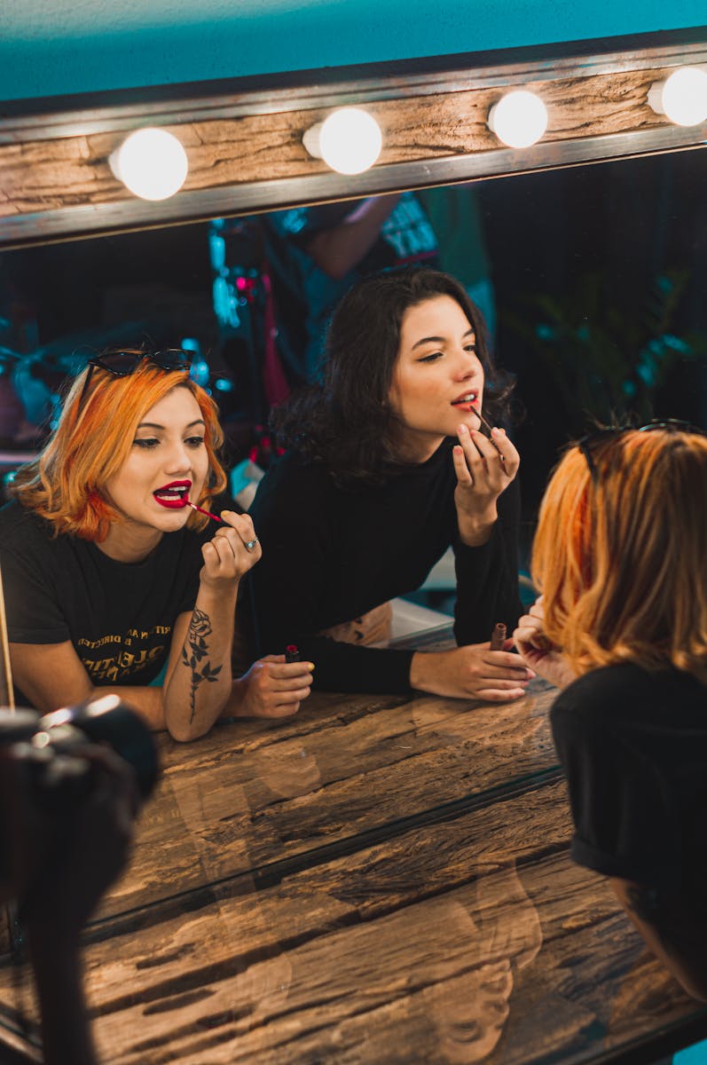 Young women enjoying makeup session in a stylish dressing room with warm lighting.