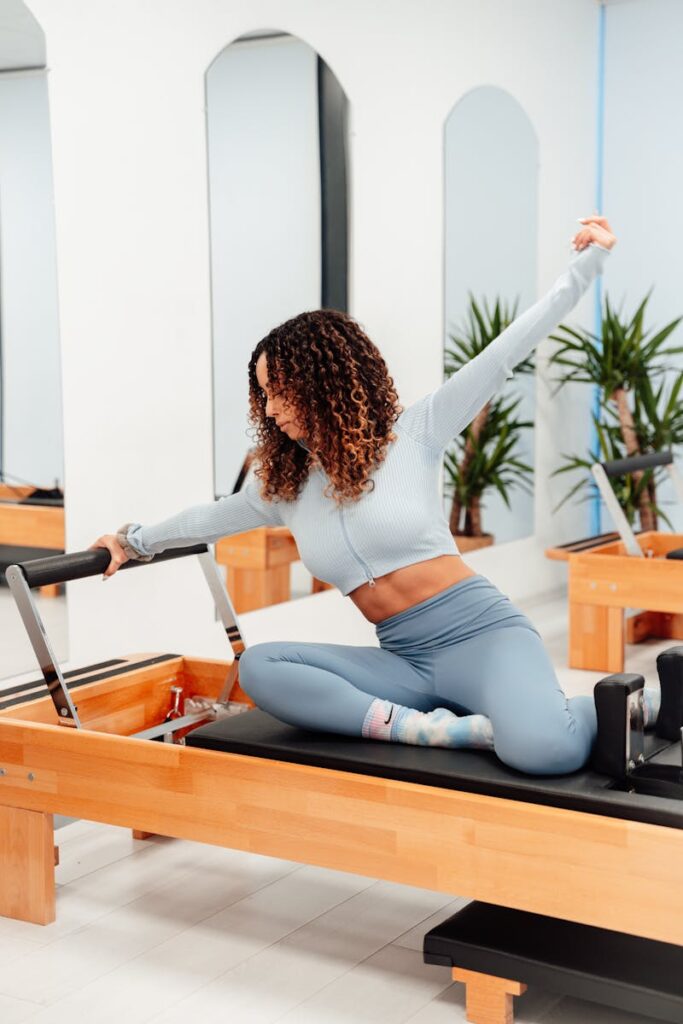 Woman with curly hair exercising on a pilates reformer in a bright fitness studio.